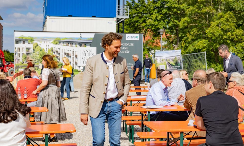Der Bürgermeister von Haar geht zwischen Bierbänken durch an denen Besucher des Spatenstichs sitzen