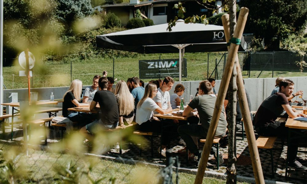 Gäste des ZIMA Sommerfest in Schwaz auf dem Vorplatz des ZIMA Projekts Minkuswiese auf Bierbänken